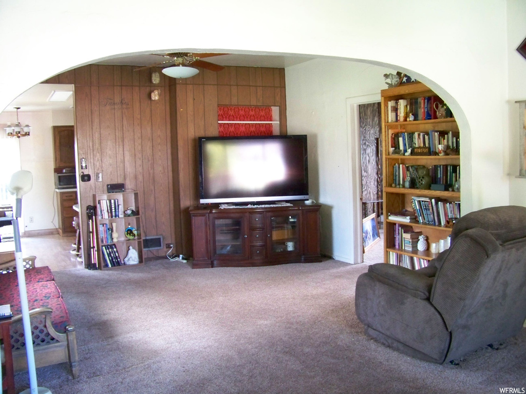 Living room featuring wooden walls, light carpet, and ceiling fan