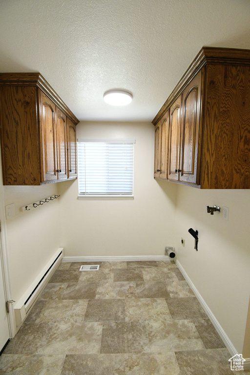 Clothes washing area with a baseboard radiator, a textured ceiling, cabinets, and light tile floors