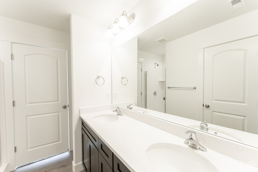 Bathroom with hardwood / wood-style flooring, large vanity, dual sinks, and walk in shower
