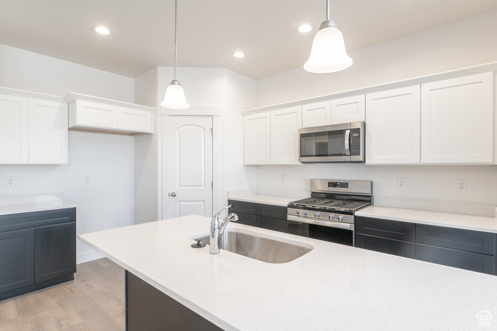 Kitchen with pendant lighting, light wood-type flooring, white cabinets, appliances with stainless steel finishes, and sink