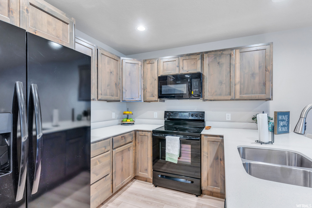 Kitchen with light countertops, black appliances, and light hardwood flooring
