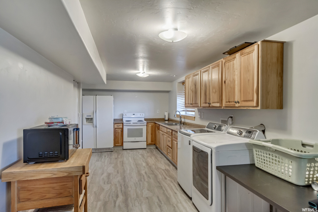 Kitchen featuring brown cabinets, washer and clothes dryer, light countertops, light hardwood floors, and white appliances