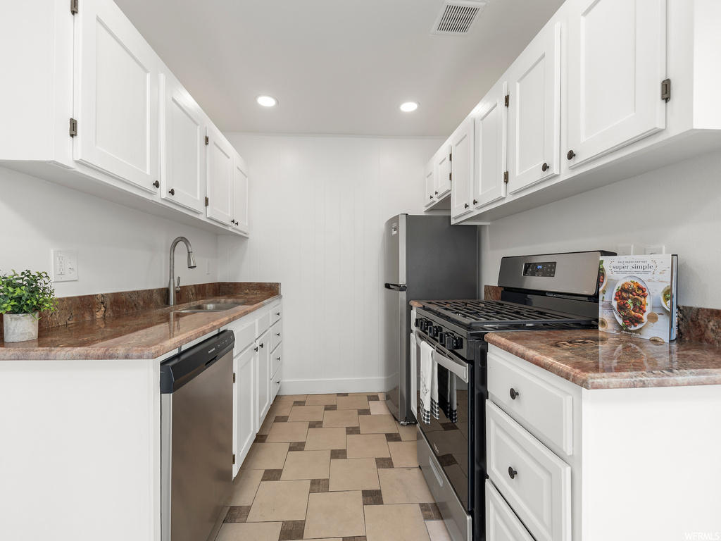 Kitchen with appliances with stainless steel finishes, white cabinetry, and light tile floors
