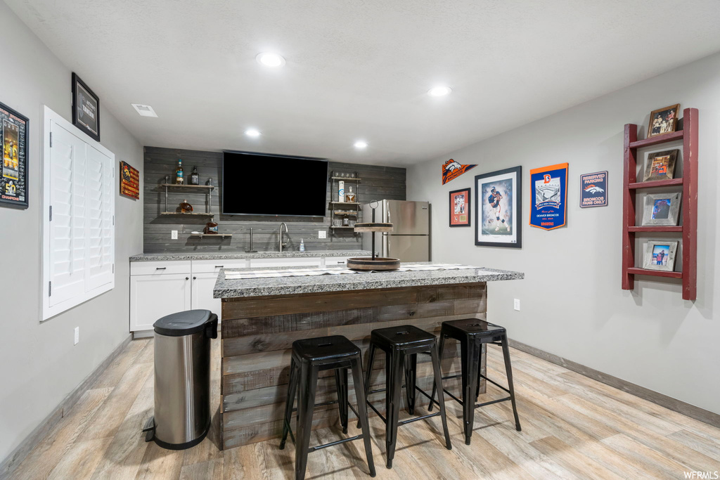 Kitchen with backsplash, light countertops, light hardwood floors, stainless steel fridge, and a center island