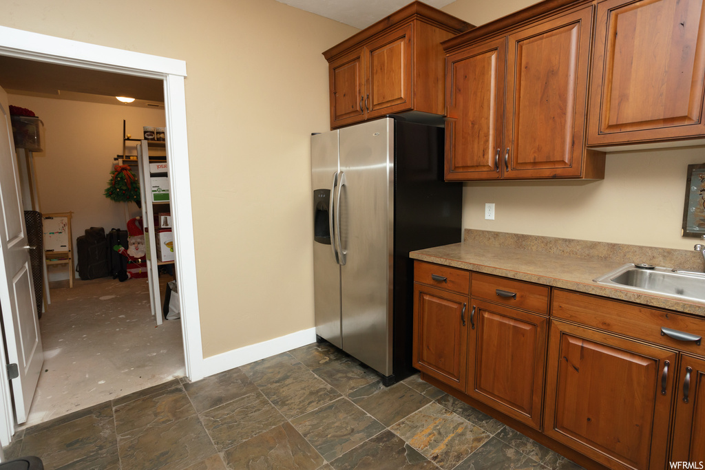 Kitchen with dark tile floors, light countertops, stainless steel fridge with ice dispenser, and brown cabinets