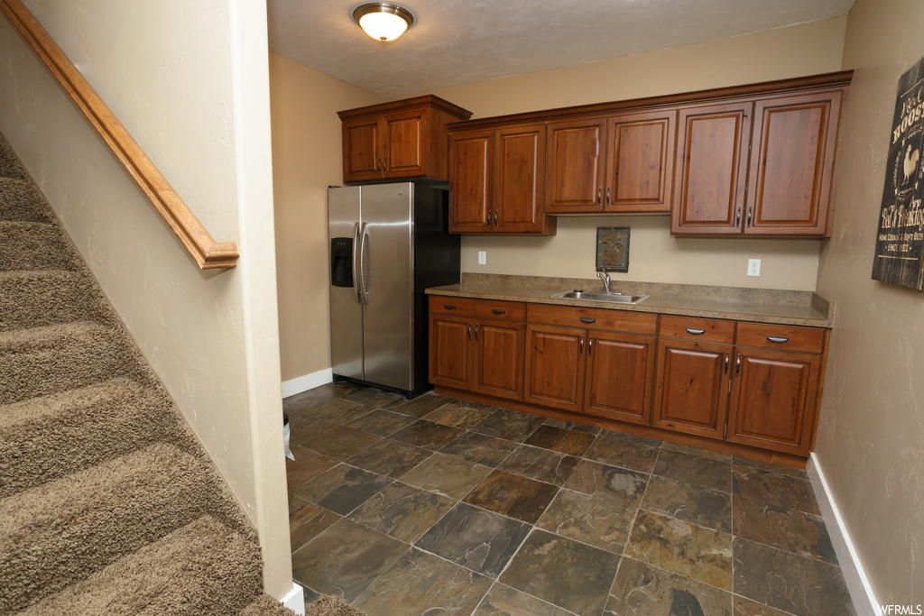 Kitchen featuring dark tile flooring, stainless steel refrigerator with ice dispenser, and brown cabinets