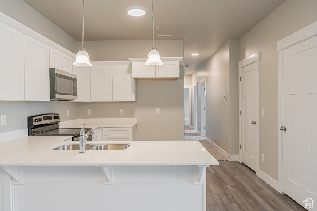 Kitchen with appliances with stainless steel finishes, white cabinets, sink, wood-type flooring, and pendant lighting