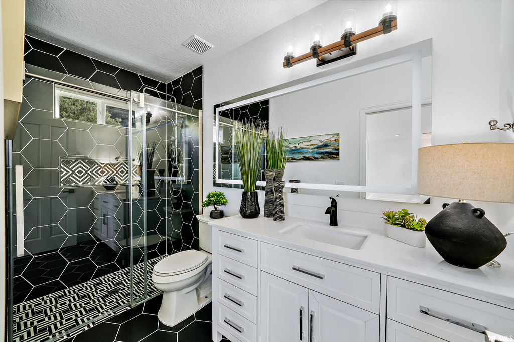 Bathroom featuring vanity, a shower with door, a textured ceiling, tile floors, and mirror