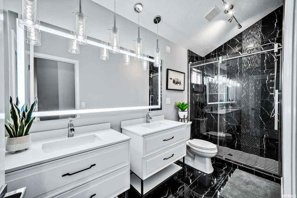 Bathroom with dual bowl vanity, mirror, a shower with shower door, and dark tile flooring