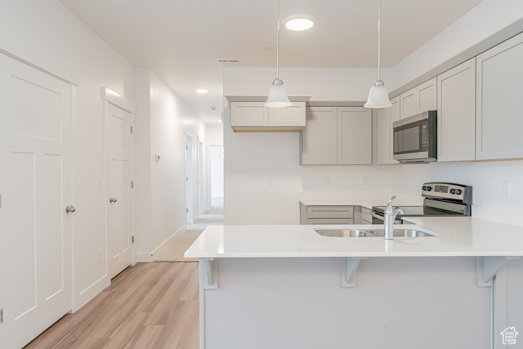 Kitchen featuring pendant lighting, a breakfast bar, kitchen peninsula, stainless steel appliances, and light hardwood / wood-style floors