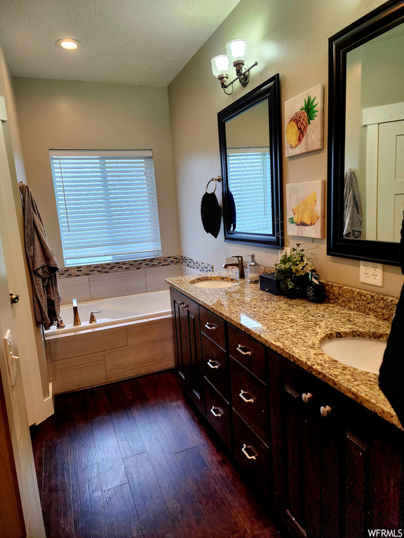 Bathroom with double vanity, mirror, tiled bath, and dark hardwood flooring