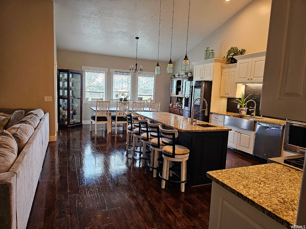 Kitchen with stovetop, black dishwasher, a textured ceiling, a center island, white cabinetry, a kitchen island with sink, dark hardwood floors, vaulted ceiling, a high ceiling, and stainless steel fridge with ice dispenser