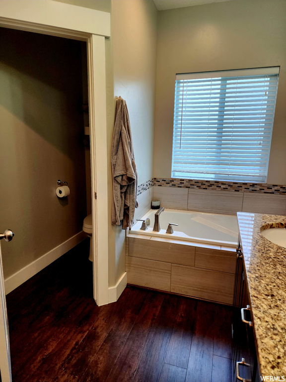 Bathroom with vanity, tiled tub, and dark hardwood floors