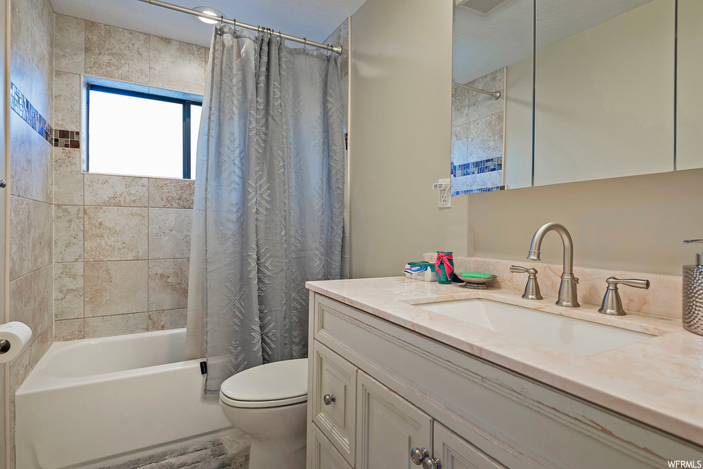 Full bathroom featuring vanity with extensive cabinet space, shower / bath combination with curtain, and toilet