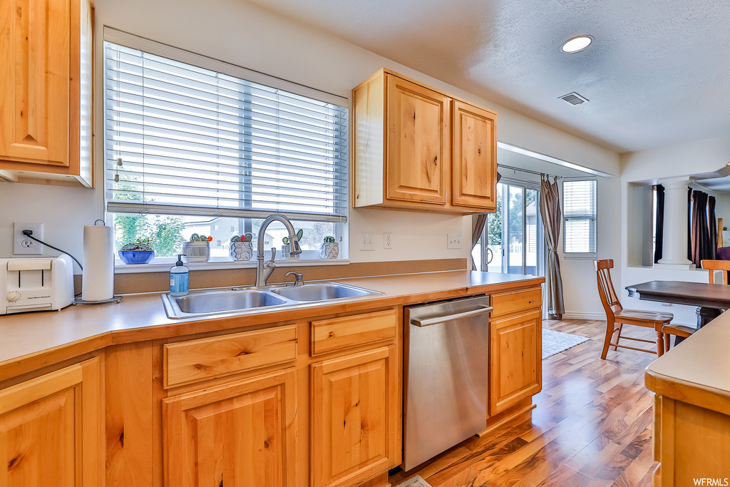 Kitchen featuring stainless steel dishwasher, plenty of natural light, brown cabinets, light countertops, and light hardwood floors