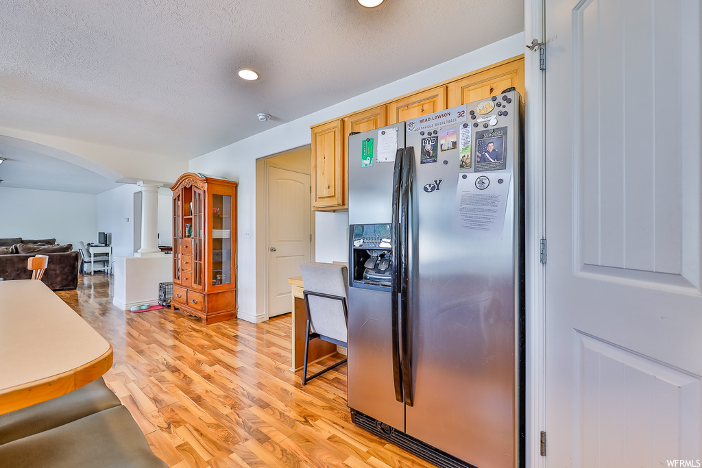 Kitchen with light hardwood flooring, a textured ceiling, and stainless steel refrigerator with ice dispenser