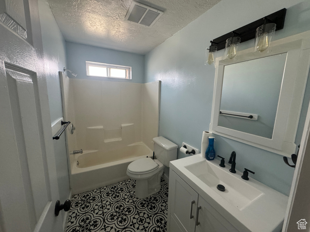 Full bathroom featuring shower / bathtub combination, tile floors, large vanity, toilet, and a textured ceiling