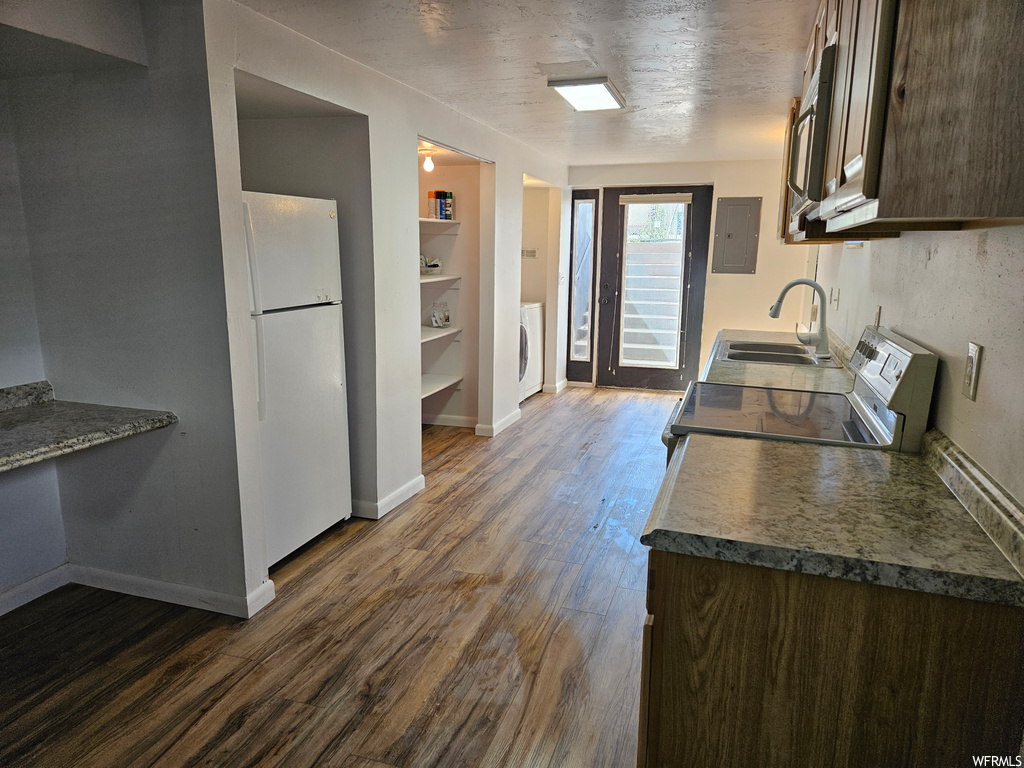Kitchen with white fridge, range, light hardwood floors, built in features, washer / dryer, and dark countertops