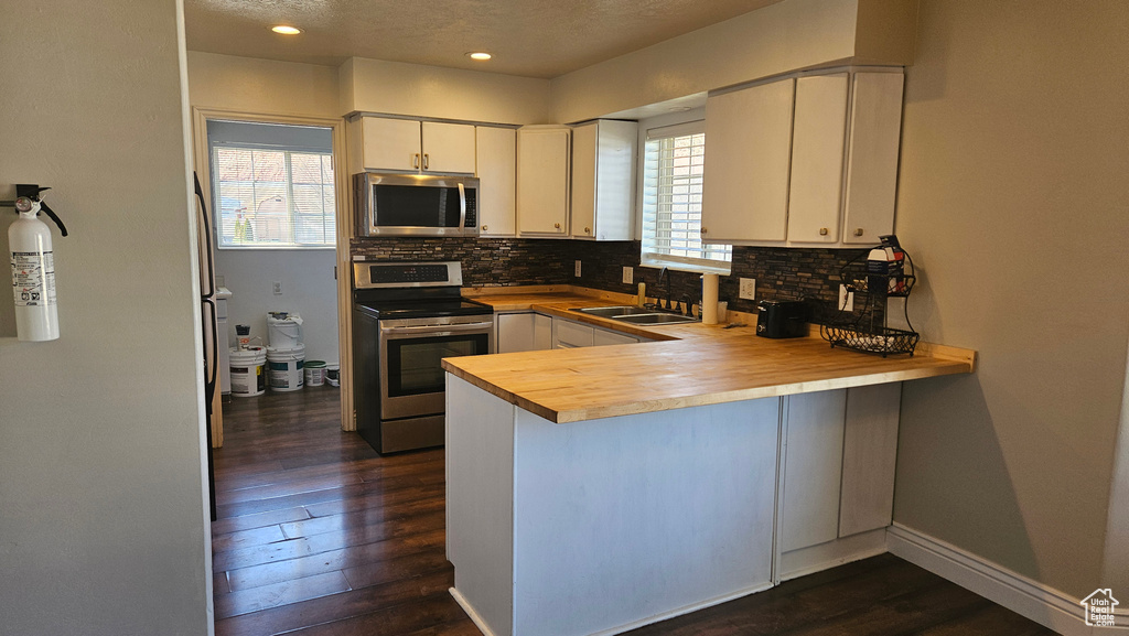 Kitchen featuring stainless steel appliances, dark hardwood / wood-style flooring, white cabinets, backsplash, and sink
