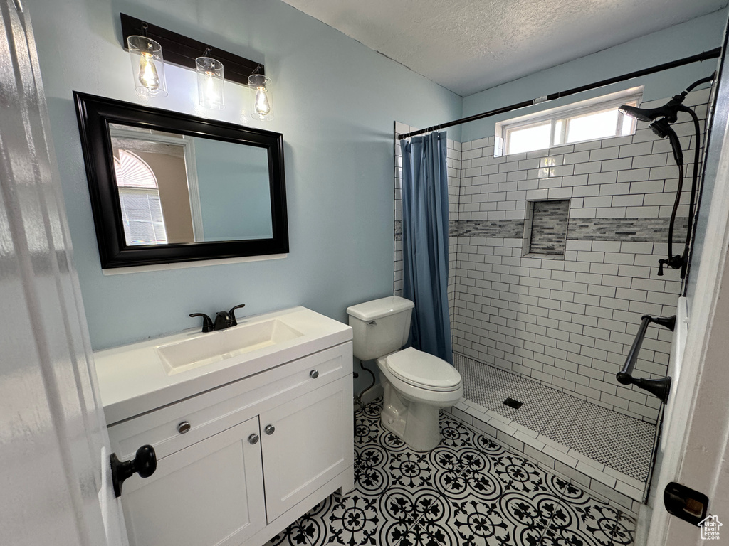 Bathroom featuring a shower with shower curtain, toilet, a textured ceiling, vanity, and tile floors