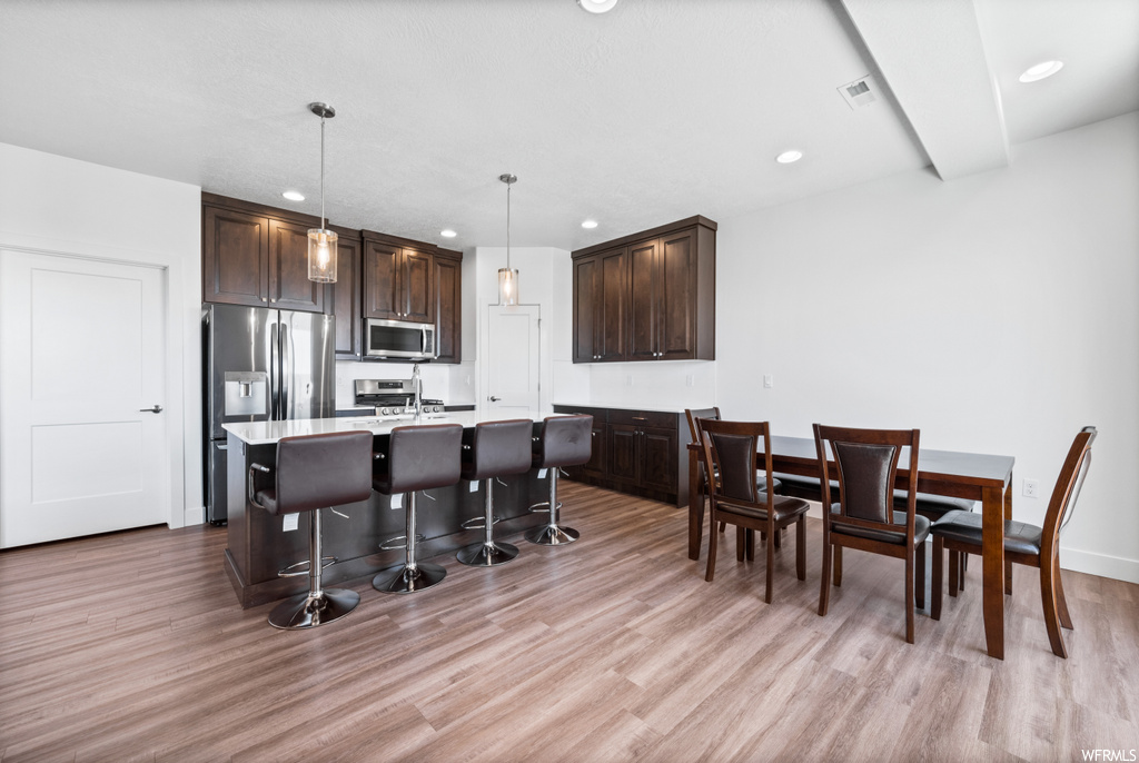Kitchen featuring hanging light fixtures, dark brown cabinets, light countertops, light hardwood floors, appliances with stainless steel finishes, and a center island