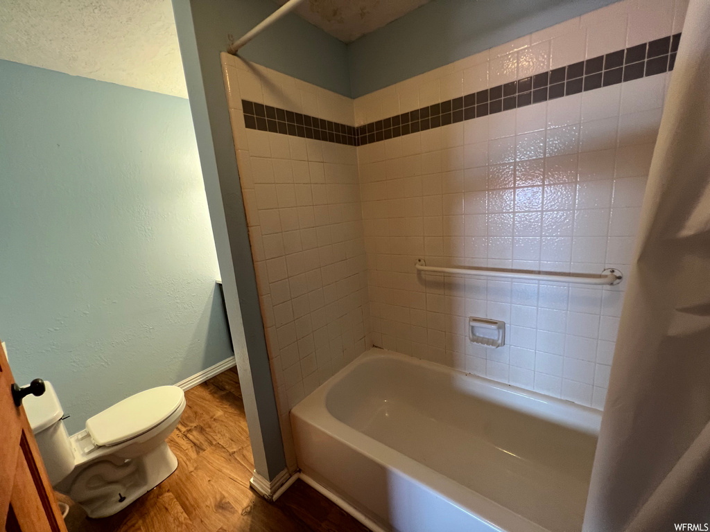 Bathroom with tiled shower / bath combo and light hardwood floors