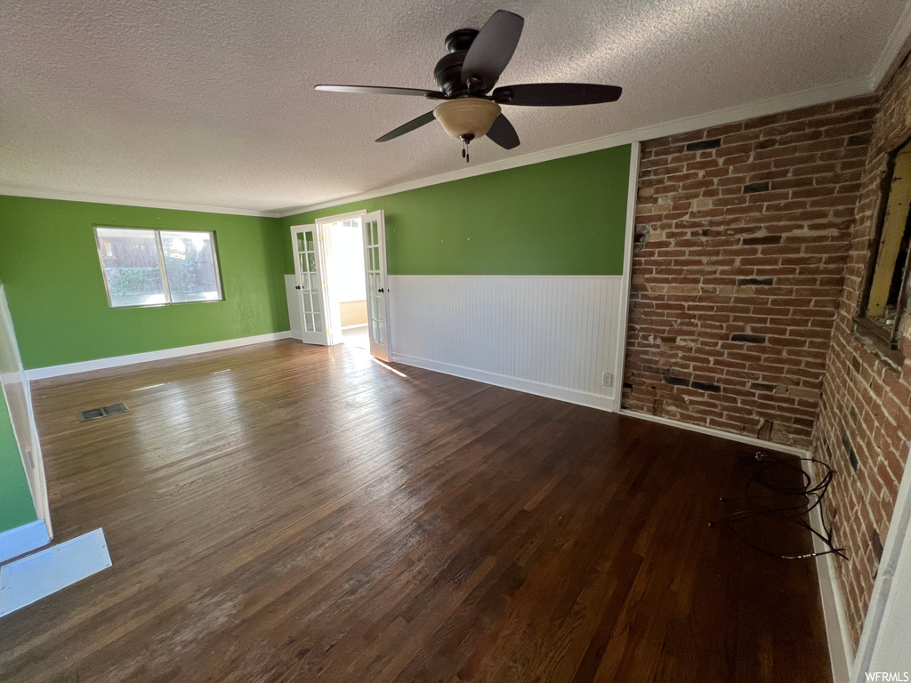 Hardwood floored spare room with ceiling fan, ornamental molding, brick wall, and a textured ceiling