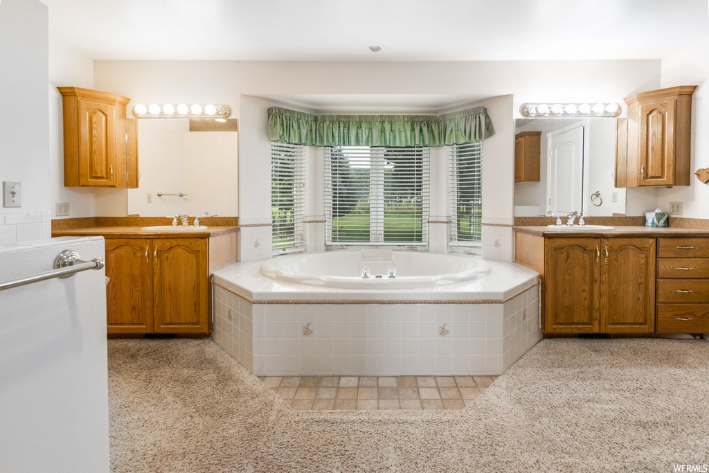Bathroom featuring tiled tub, mirror, and dual large bowl vanity