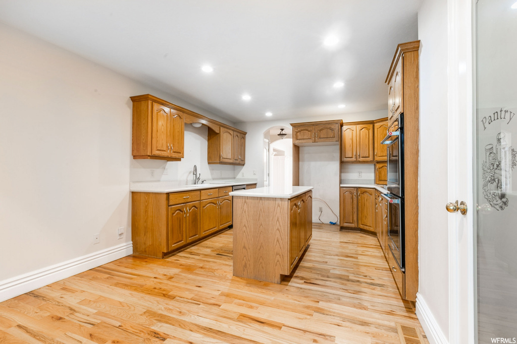 Kitchen featuring stainless steel oven, brown cabinets, light countertops, and light hardwood floors
