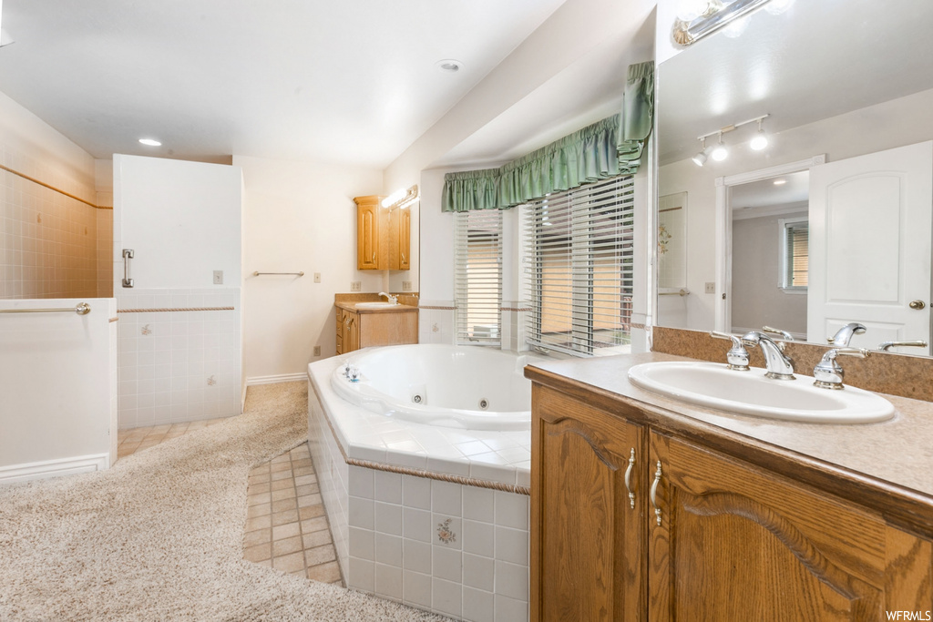 Bathroom featuring oversized vanity, a healthy amount of sunlight, mirror, and tiled bath