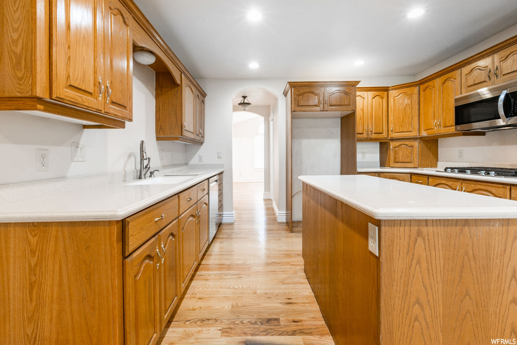 Kitchen with light hardwood flooring, stainless steel appliances, light countertops, and brown cabinets