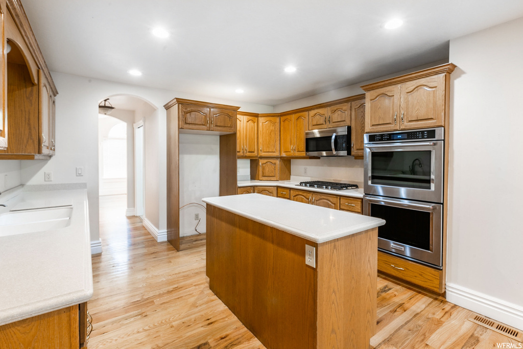 Kitchen with light countertops, brown cabinets, light hardwood floors, and stainless steel appliances