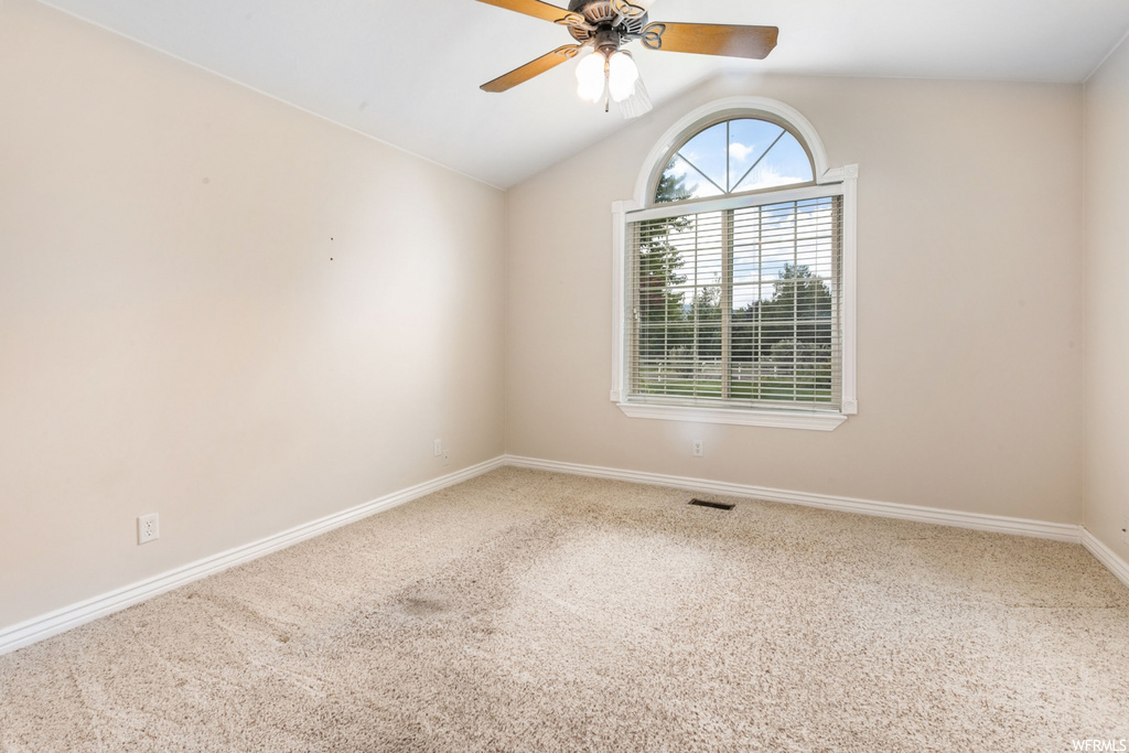 Spare room featuring light carpet, lofted ceiling, and ceiling fan