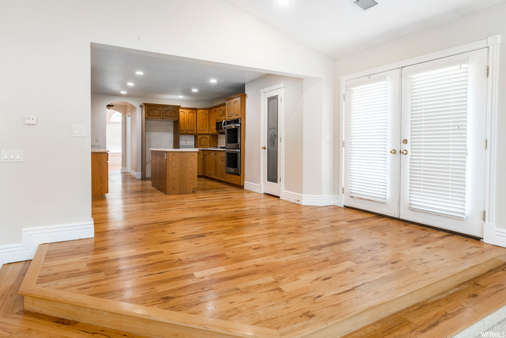 Kitchen with stainless steel double oven, lofted ceiling, french doors, brown cabinets, and light hardwood floors