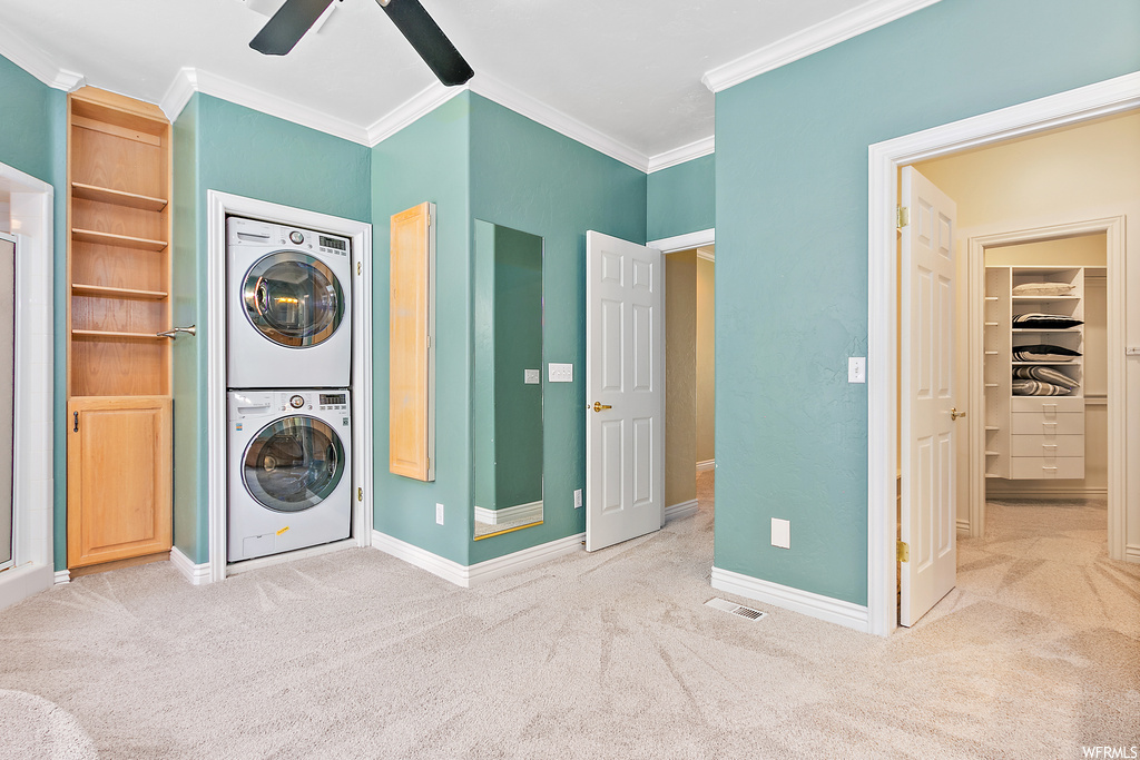 Clothes washing area featuring stacked washer / dryer, crown molding, light carpet, and ceiling fan