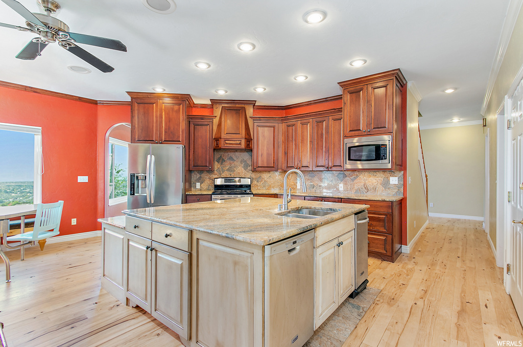 Kitchen featuring ornamental molding, backsplash, light hardwood floors, custom exhaust hood, stainless steel appliances, and light stone counters