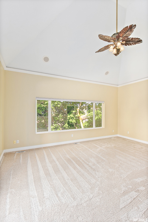 Carpeted empty room featuring crown molding, lofted ceiling, a healthy amount of sunlight, and ceiling fan
