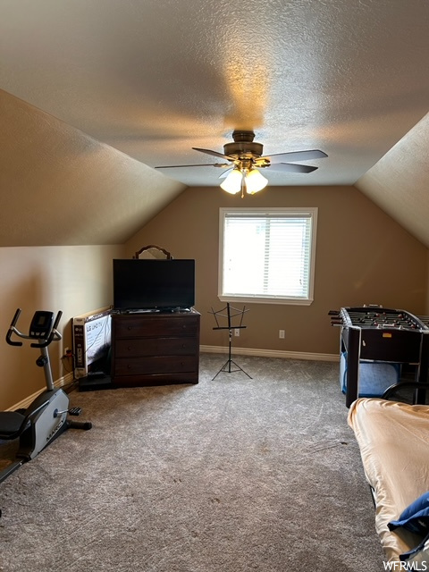 Carpeted bedroom featuring a textured ceiling, vaulted ceiling, and ceiling fan