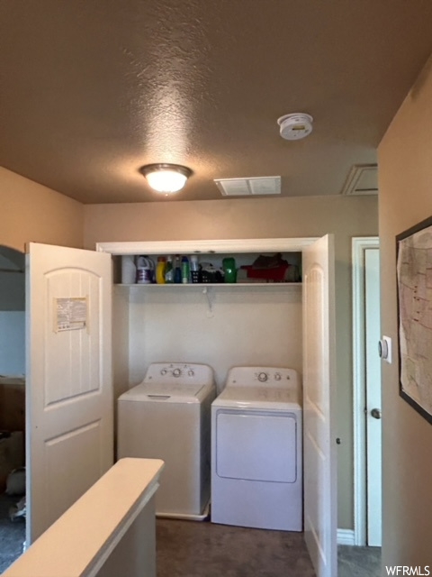Laundry room featuring dark carpet, washer and clothes dryer, and a textured ceiling