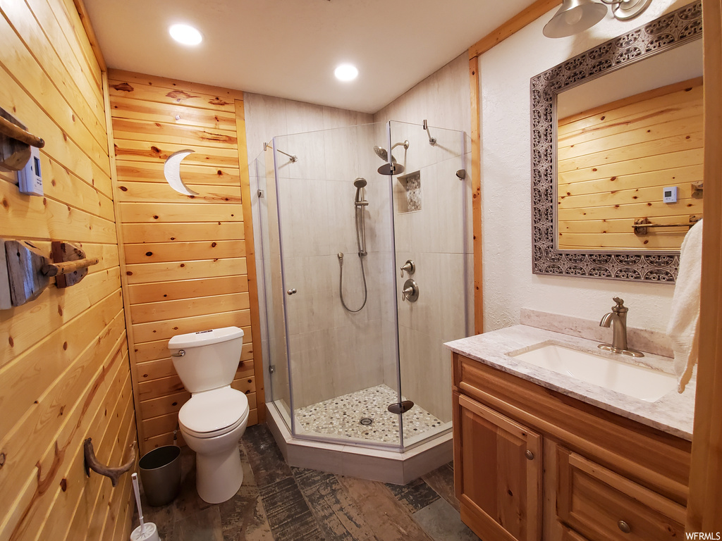 Bathroom with vanity, an enclosed shower, mirror, dark tile flooring, and wood walls