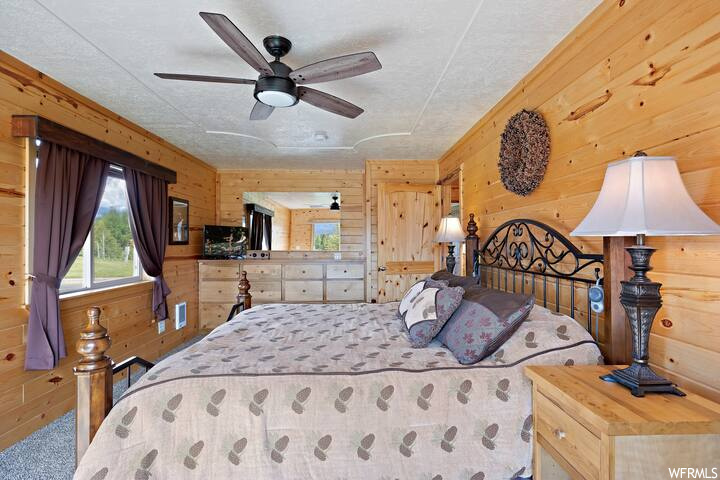 Bedroom with wooden walls, light carpet, and ceiling fan