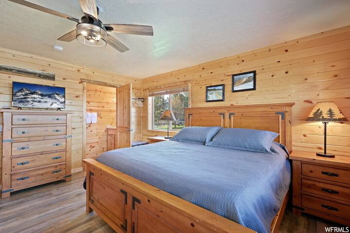 Hardwood floored bedroom with wooden walls and ceiling fan