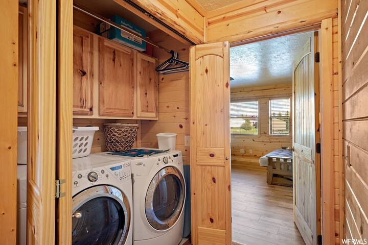 Laundry room featuring wood walls, washing machine and clothes dryer, and light hardwood floors