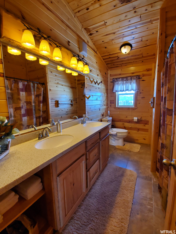 Bathroom with mirror, dual large vanity, wooden walls, dark tile flooring, lofted ceiling, and wood ceiling