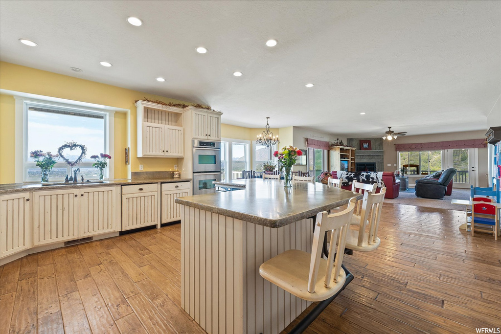 Kitchen with a kitchen island with sink, a center island, stainless steel double oven, light hardwood floors, and ceiling fan
