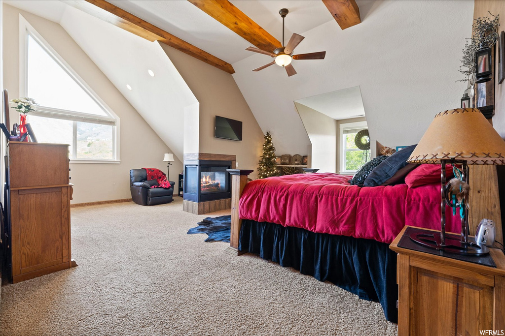 Carpeted bedroom featuring vaulted ceiling with beams, a fireplace, and ceiling fan