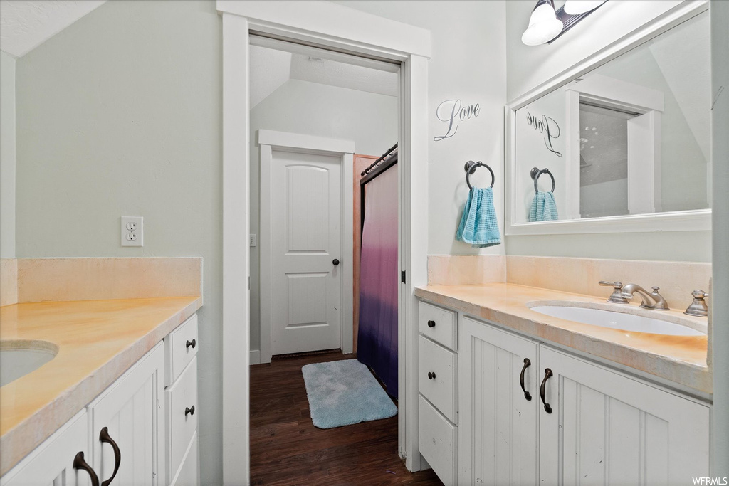 Bathroom with lofted ceiling, double sink vanity, mirror, and dark hardwood flooring