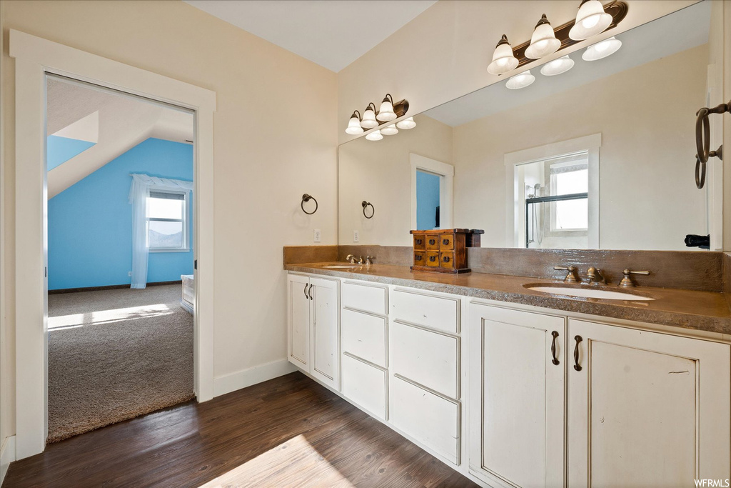 Bathroom featuring dark hardwood floors, vaulted ceiling, mirror, and dual bowl vanity