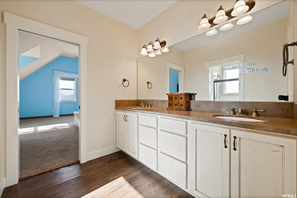 Bathroom with mirror, double sink vanity, lofted ceiling, and dark hardwood floors