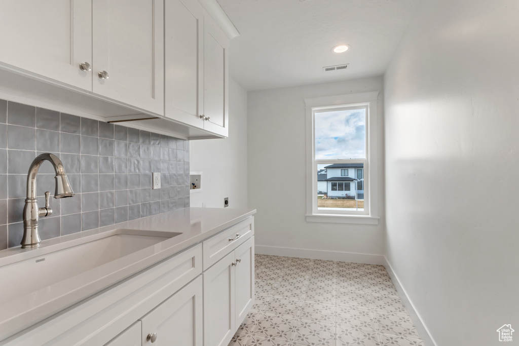 Kitchen featuring sink, white cabinets, backsplash, and light tile floors